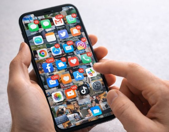 A person's hand holding a smartphone with a screen chaotically filled with app icons and notifications, illustrating the visual stress of digital clutter.